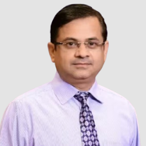Professional head-and-shoulders portrait of a man wearing glasses, a light purple shirt, and a patterned tie, against a neutral gray background.