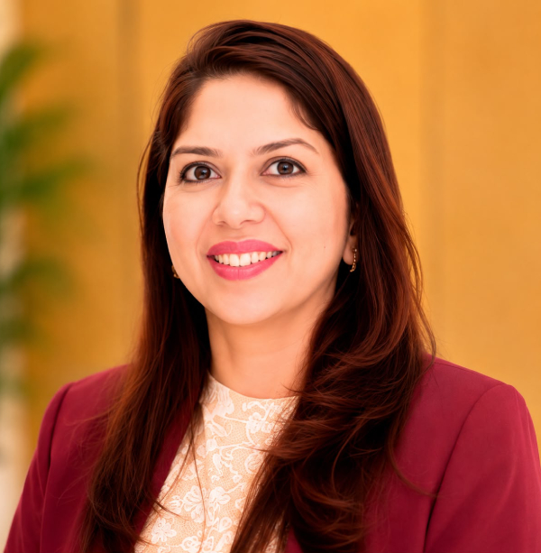 Head-and-shoulders portrait of a smiling woman with long brown hair, wearing a burgundy blazer and a lace blouse in a warm indoor setting